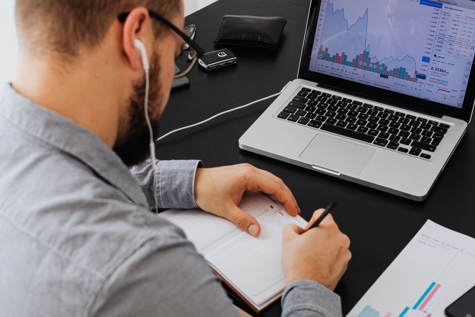 Cibersegurança Corporativa — A businessman analyzing stock data on a laptop while taking notes at a desk.