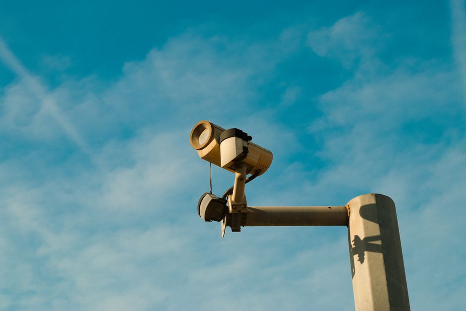 Cibersegurança Corporativa — A surveillance camera mounted outdoors against a bright blue sky, symbolizing security and
